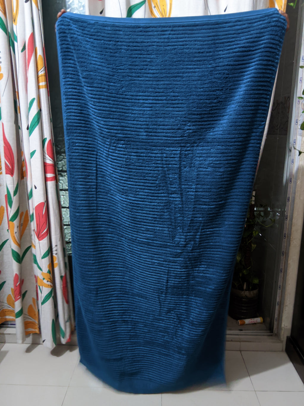 Blue textured bath towel draped over a chair with colorful curtains in the background