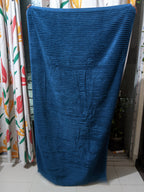 Blue textured bath towel draped over a chair with colorful curtains in the background