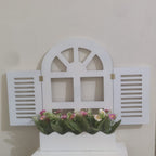 Decorative white window frame with flowers on a shelf against a beige wall.